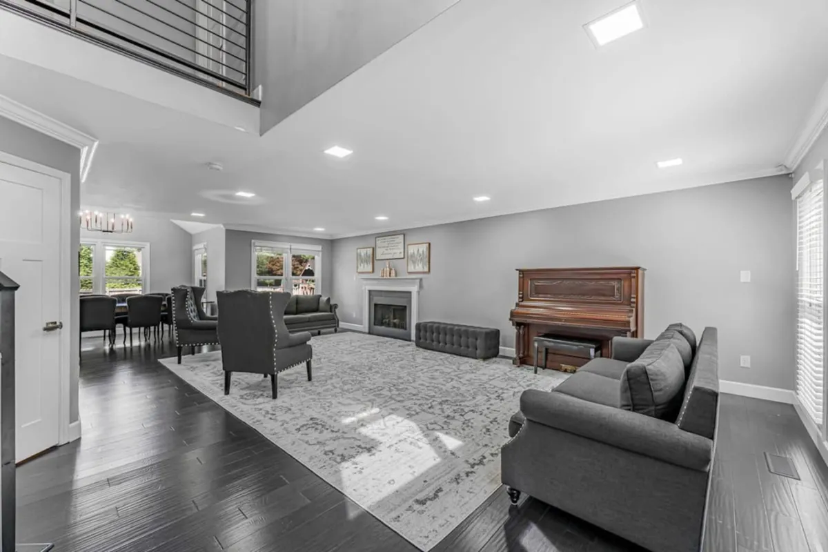A spacious, elegant interior featuring a grand piano, a cozy fireplace, a comfortable sofa set, and a dining area in view. The open layout allows for seamless movement between living and dining spaces, with the piano as a focal point inviting musical moments.
