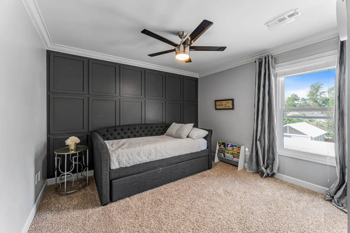 This image captures a peaceful, multi-purpose nook with a daybed adorned with decorative pillows, a dark paneled accent wall, and a large window with curtains. The space is tranquil and comfortable, ideal for reading, relaxing, or quiet study sessions.