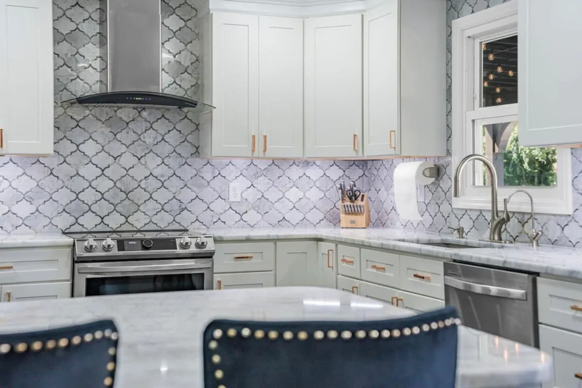 A modern kitchen with a marble countertop, decorative backsplash, stainless steel appliances, and a kitchen island. The space is clearly designed for both meal preparation and social interaction, with enough room to gather around for conversations or group cooking.