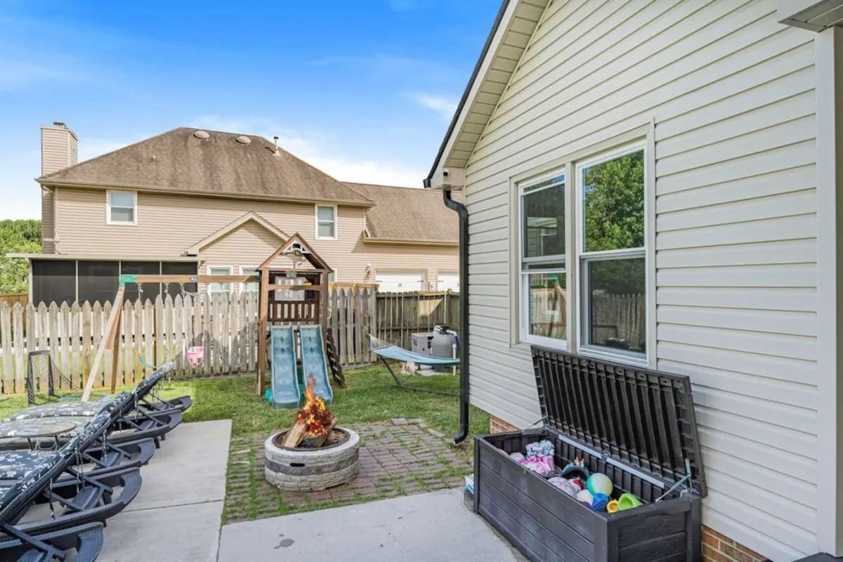 An inviting outdoor area with a fire pit, play structure, storage bench, and lawn chairs. Children are playing, and there’s a sense of togetherness as the sun sets, making the space ideal for evening gatherings and roasting s'mores.
