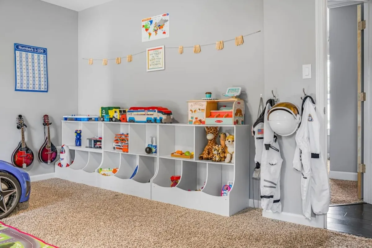 This image displays a dedicated play space with a toy storage unit, guitars, and an assortment of children’s toys and costumes, including space suits. The scene radiates creativity and fun, inviting kids to explore and play.