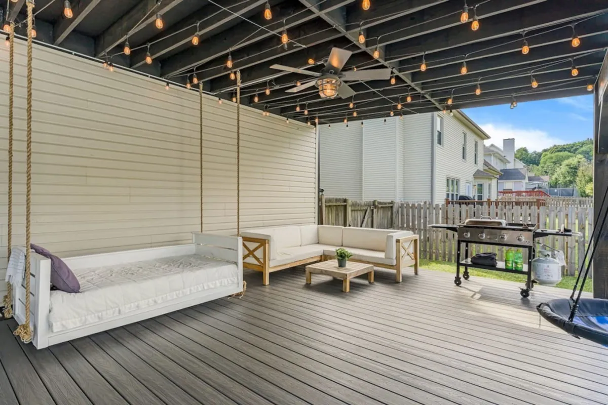 A stylish covered porch with swing seating, an outdoor sofa, a grill, and hanging string lights, setting the scene for relaxed outdoor living. The layout hints at spaces for both lounging and alfresco dining, with the grill visible to underscore outdoor cooking appeal.