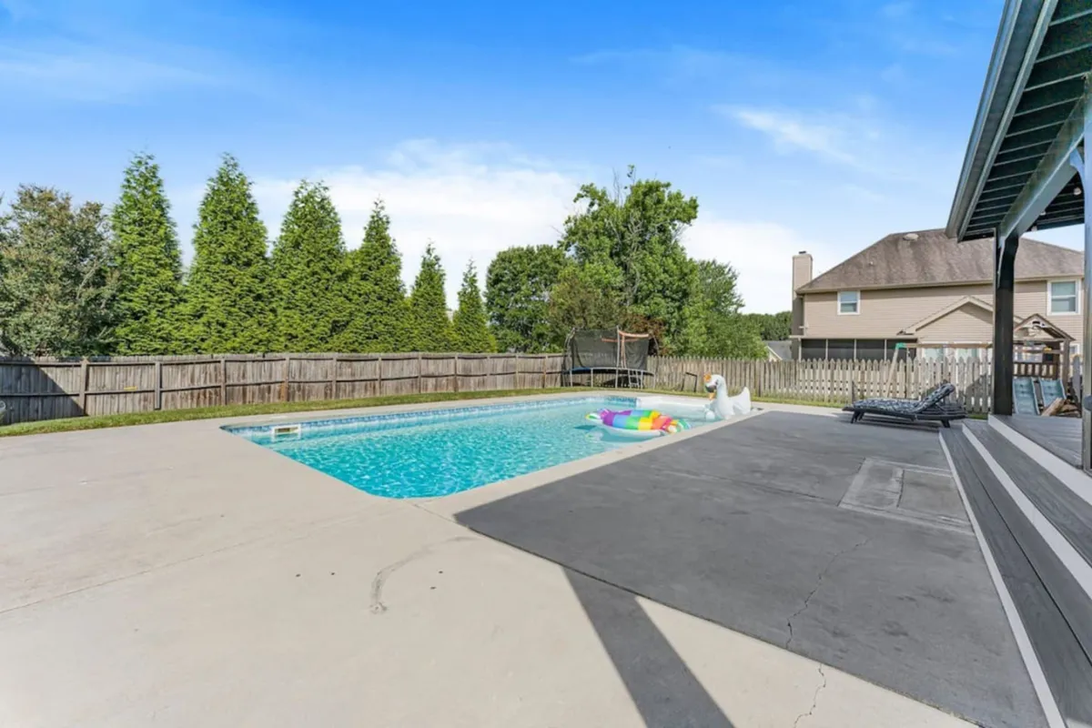 A vibrant backyard with a sparkling swimming pool, colorful pool floats, green trees, and a fenced yard. The space radiates energy and joy, evoking summertime fun, pool parties, and outdoor gatherings for all ages.